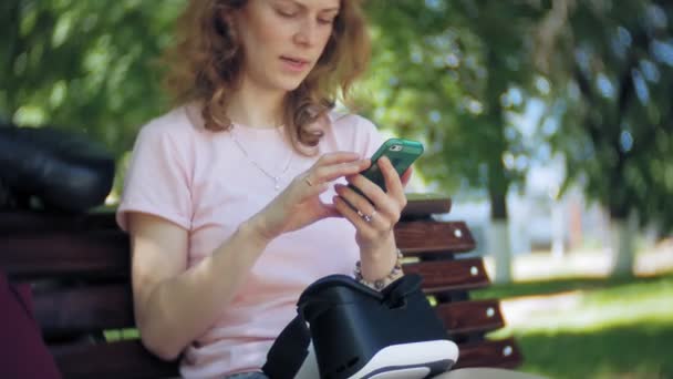 若い女性は、公園でヘッドマウントディス プレイを使用します。スマート フォン用 Vr ヘルメットを使用して遊ぶゲーム。幸せです — ストック動画