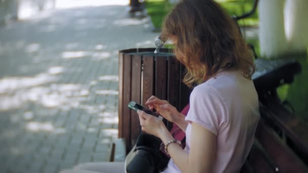 Mujer joven utiliza la pantalla montada en la cabeza en el parque. Jugar a juego con casco VR para teléfonos inteligentes. Feliz. — Vídeos de Stock