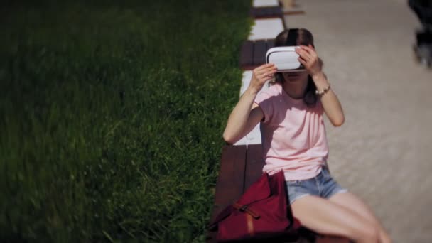 Wanita muda menggunakan head-mounted display di taman. Bermain game menggunakan VR-helm untuk ponsel pintar. Selamat. — Stok Video