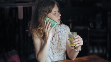 bir kadın bir restoranda bir kokteyl içer ve telefon kullanır