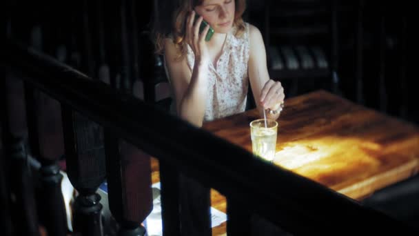 Uma mulher bebe um cocktail num restaurante e usa o telefone — Vídeo de Stock