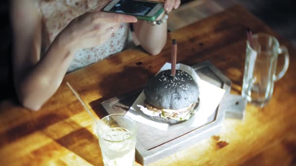 Mujer joven comiendo comida rápida, hamburguesa negra — Vídeos de Stock