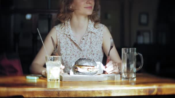 Jonge vrouw eten fastfood, zwarte hamburger — Stockvideo