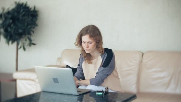 Молода красива бізнес-леді сидить на дивані за столом з планшетом — стокове відео