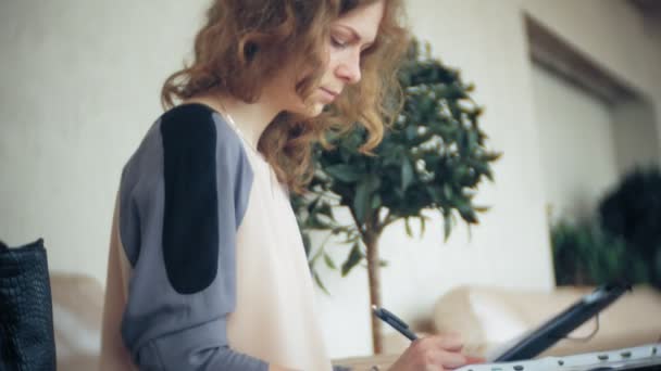 Jonge mooie zakenvrouw zittend op de Bank aan tafel met tablet en op zoek via papier — Stockvideo