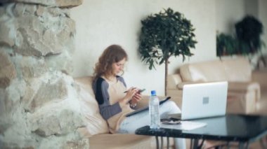 Divan tablet ile masada oturan ve smartphone kullanarak genç güzel iş kadını