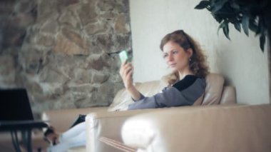 Divan tablet ile masada oturan ve smartphone kullanarak genç güzel iş kadını