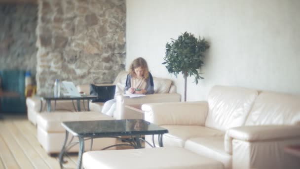 Young beautiful business woman sitting on sofa at table with tablet and using smartphone — Stock Video