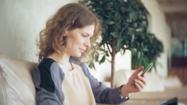 Joven mujer de negocios hermosa sentado en el sofá en la mesa con la tableta y el uso de teléfono inteligente — Vídeos de Stock