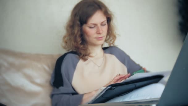 Ung vacker affärskvinna sitter på soffan vid bord med tablett och titta igenom papper — Stockvideo
