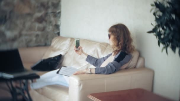 Tânără frumoasă femeie de afaceri care stă pe canapea la masă cu tabletă și folosind smartphone — Videoclip de stoc