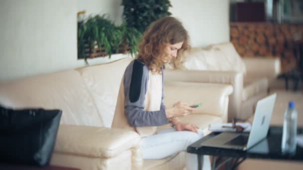 年轻漂亮的商业妇女坐在沙发上的平板电脑和看通过纸 — 图库视频影像