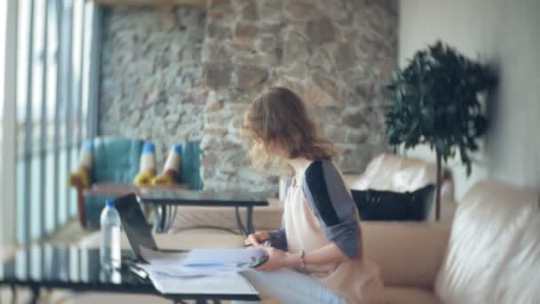Divan tablet ile masada oturan ve kağıt arıyor genç güzel iş kadını — Stok video
