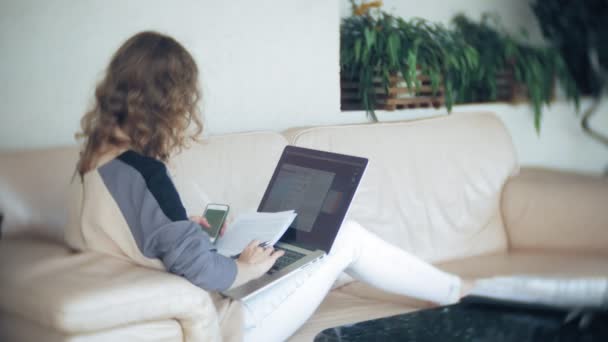 Молодая красивая деловая женщина сидит на диване за столом с планшетом и смотрит через бумагу — стоковое видео