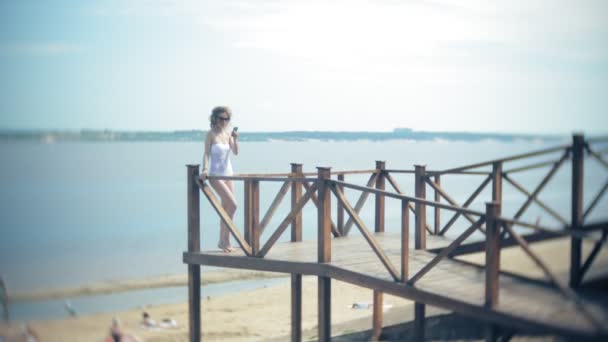 Hete meisje permanent op het strand op de brug in de zon. 4k. — Stockvideo