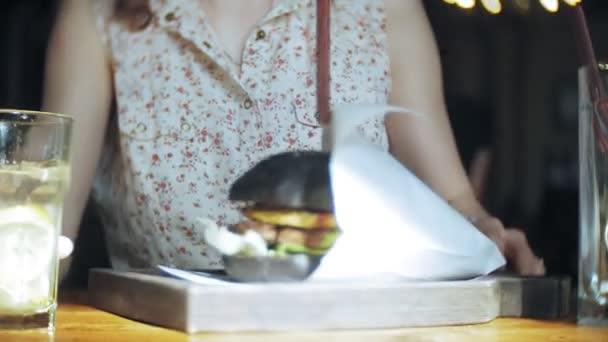 Mujer joven comiendo comida rápida, hamburguesa negra — Vídeos de Stock