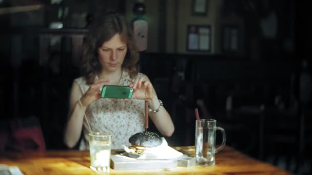 Mujer joven comiendo comida rápida, hamburguesa negra — Vídeos de Stock