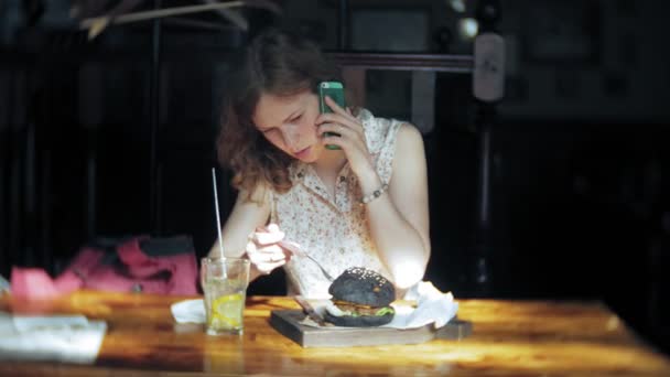 Молодая женщина ест фаст-фуд, черный гамбургер — стоковое видео