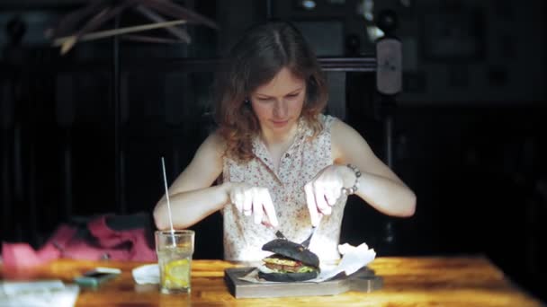 Mujer joven comiendo comida rápida, hamburguesa negra — Vídeo de stock