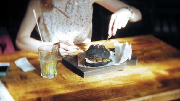 Fiatal nő evés gyorsétterem, fekete hamburger — Stock videók