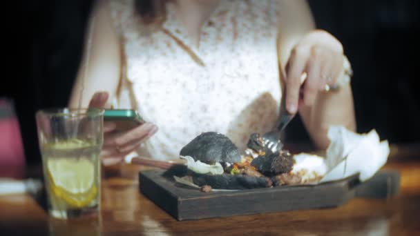 Молодая женщина ест фаст-фуд, черный гамбургер — стоковое видео