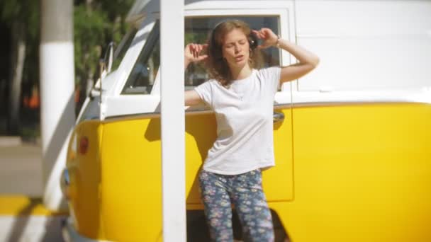 黄色のヴァゴン車音楽を聴くヘッドフォン スマート フォンを使用して -、リラックスを楽しむ、技術の旅行の概念ごと屋外に若い女性 — ストック動画