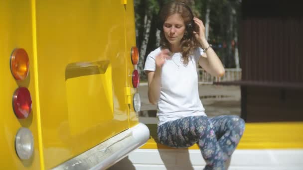 Mujer joven al aire libre por vagón amarillo coche escuchar música en los auriculares con el teléfono inteligente - relajarse, disfrutar, concepto de la tecnología y viajar — Vídeo de stock