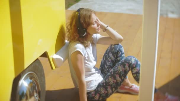 Mujer joven al aire libre por vagón amarillo coche escuchar música en los auriculares con el teléfono inteligente - relajarse, disfrutar, concepto de la tecnología y viajar — Vídeo de stock