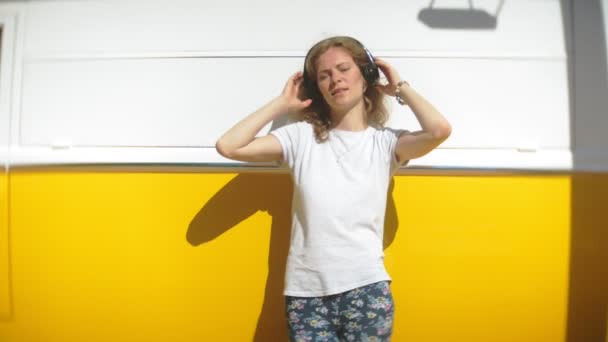 Mujer joven al aire libre por vagón amarillo coche escuchar música en los auriculares con el teléfono inteligente - relajarse, disfrutar, concepto de la tecnología y viajar — Vídeo de stock