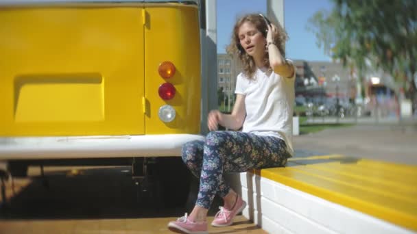 Jonge vrouw buitenshuis door gele vagon auto luisteren muziek hoofdtelefoon using smartphone - ontspannen, genieten, concept van technologie en reizen — Stockvideo