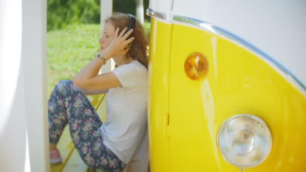 年轻女子户外由黄色 vagon 汽车在耳机中收听音乐使用智能手机-放松, 享受, 技术和旅行的概念 — 图库视频影像