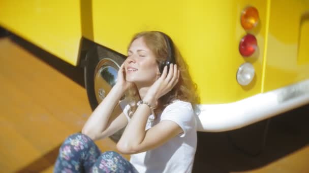 Ung kvinna Utomhus vid gula vagon bil lyssnar musik i hörlurar använder smartphone - avslappnande, njuter, begreppet teknik och resor — Stockvideo