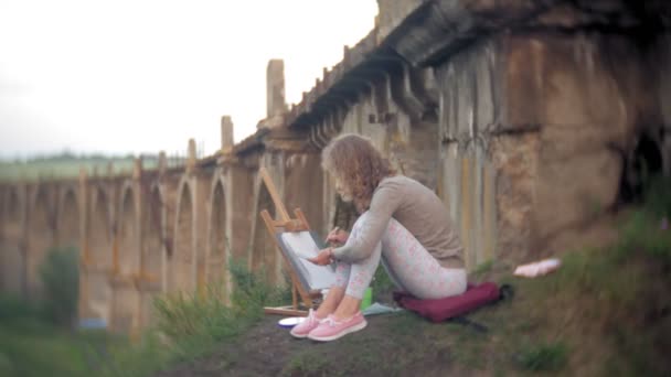 Jovem mulher se baseia nas tintas cavalete e escova velha ponte vintage — Vídeo de Stock