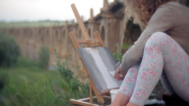 Jeune femme dessine sur le chevalet peintures et brosse vieux pont vintage — Video