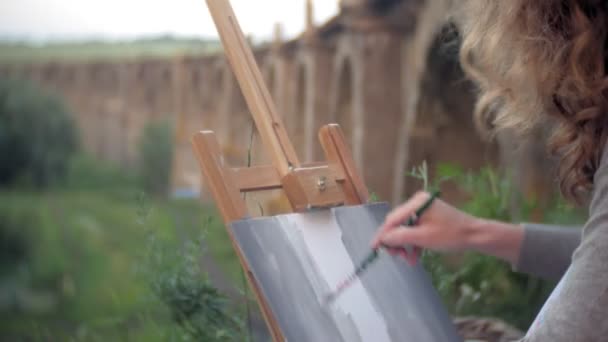 Ung kvinna bygger på staffli målarfärg och pensel gamla vintage bridge — Stockvideo