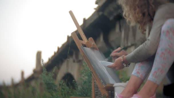 Jovem mulher se baseia nas tintas cavalete e escova velha ponte vintage — Vídeo de Stock