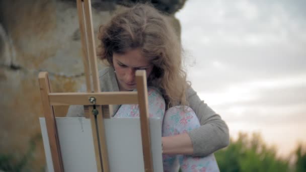 Mujer joven se basa en las pinturas de caballete y cepillo viejo puente vintage — Vídeos de Stock