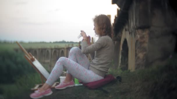 Young woman draws on the easel paints and brush old vintage bridge — Stock Video