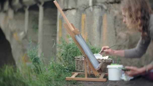 Ung kvinna bygger på staffli målarfärg och pensel gamla vintage bridge — Stockvideo