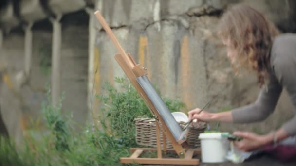 Jeune femme dessine sur le chevalet peintures et brosse vieux pont vintage — Video