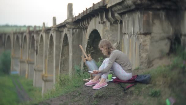 Giovane donna disegna sul cavalletto vernici e pennello vecchio ponte d'epoca — Video Stock