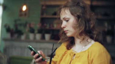 Genç bir kadın bir kafe barda bir kokteyl içiyor ve bir telefon kullanır