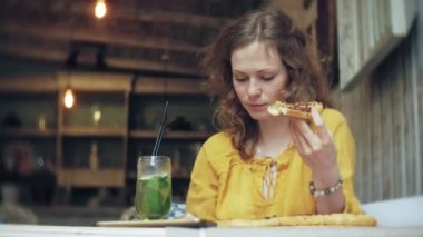 Genç bir kadın bir kafe barda bir pasta yiyor ve bir telefon kullanır