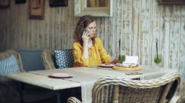 Genç bir kadın bir kafe barda bir kokteyl içiyor ve bir telefon kullanır