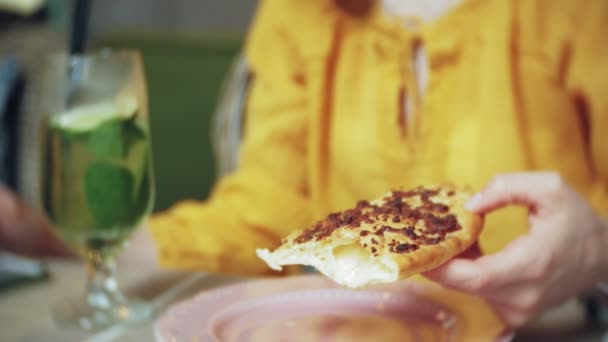 Μια νεαρή γυναίκα τρώει μια πίτα σε ένα καφέ-μπαρ και χρησιμοποιεί ένα τηλέφωνο — Αρχείο Βίντεο