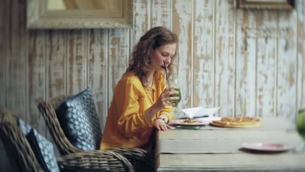 Uma jovem come uma torta em um café bar e usa um telefone — Vídeo de Stock