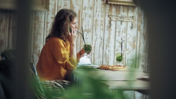 Mladá žena pije koktejl v café baru a používá telefon — Stock video