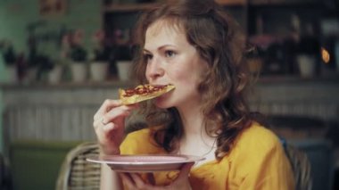 Genç bir kadın bir kafe barda bir pasta yiyor ve bir telefon kullanır