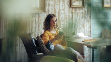 Genç bir kadın bir kafe barda bir kokteyl içiyor ve bir telefon kullanır