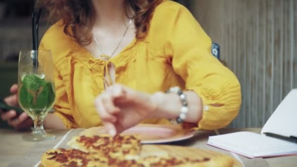 Eine junge Frau isst in einer Cafébar eine Torte und benutzt ein Telefon — Stockvideo